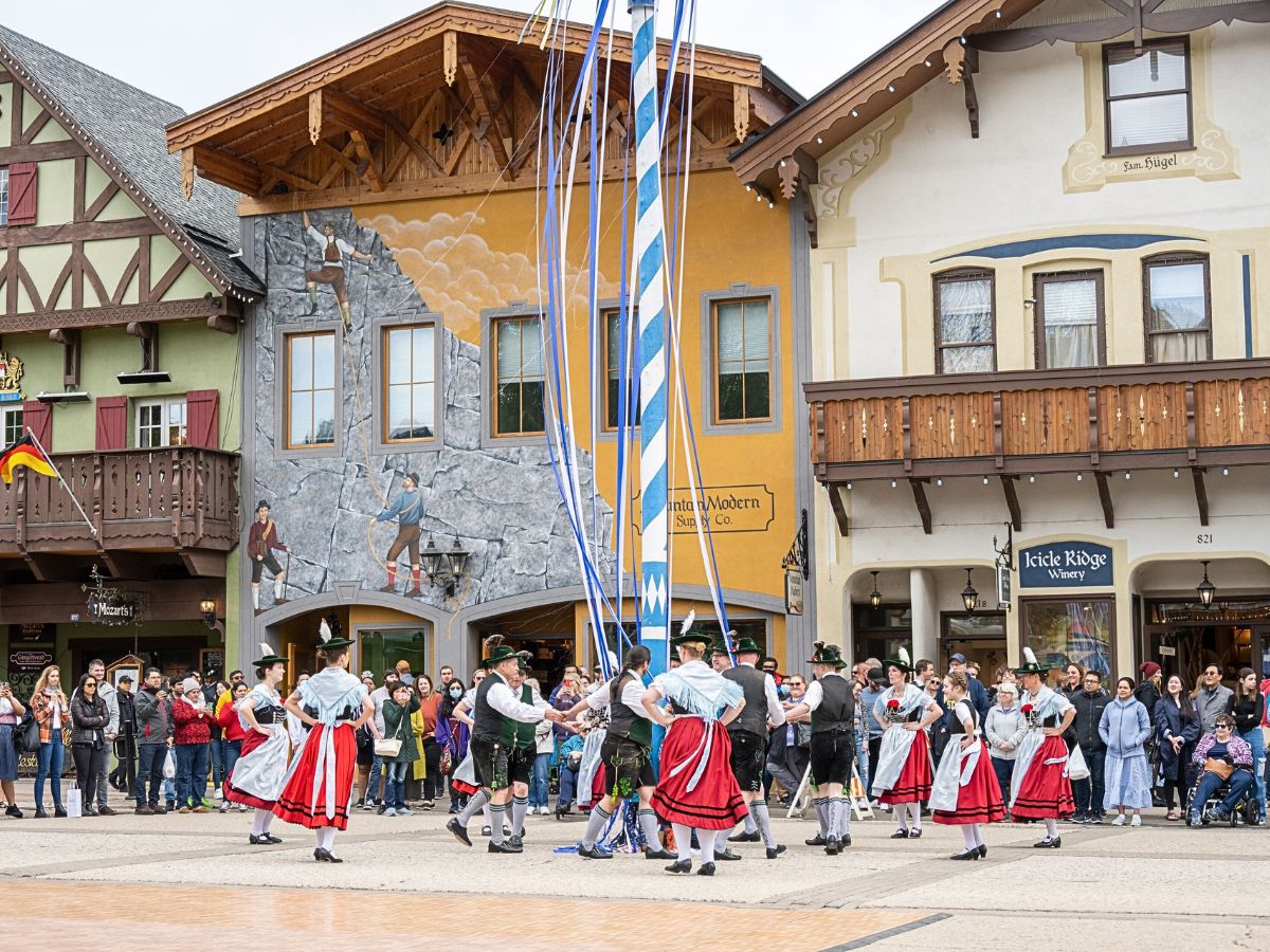 The traditional Maifest celebration in Leavenworth, Washington. A group of dancers in Bavarian-style outfits is performing around a maypole adorned with blue and white ribbons, while a crowd gathers to watch. The colorful, Alpine-inspired buildings in the background add to the festive atmosphere. Maifest, held in spring, is a lively cultural event that showcases the town’s German heritage, making it one of the best times to visit Leavenworth for an authentic experience.