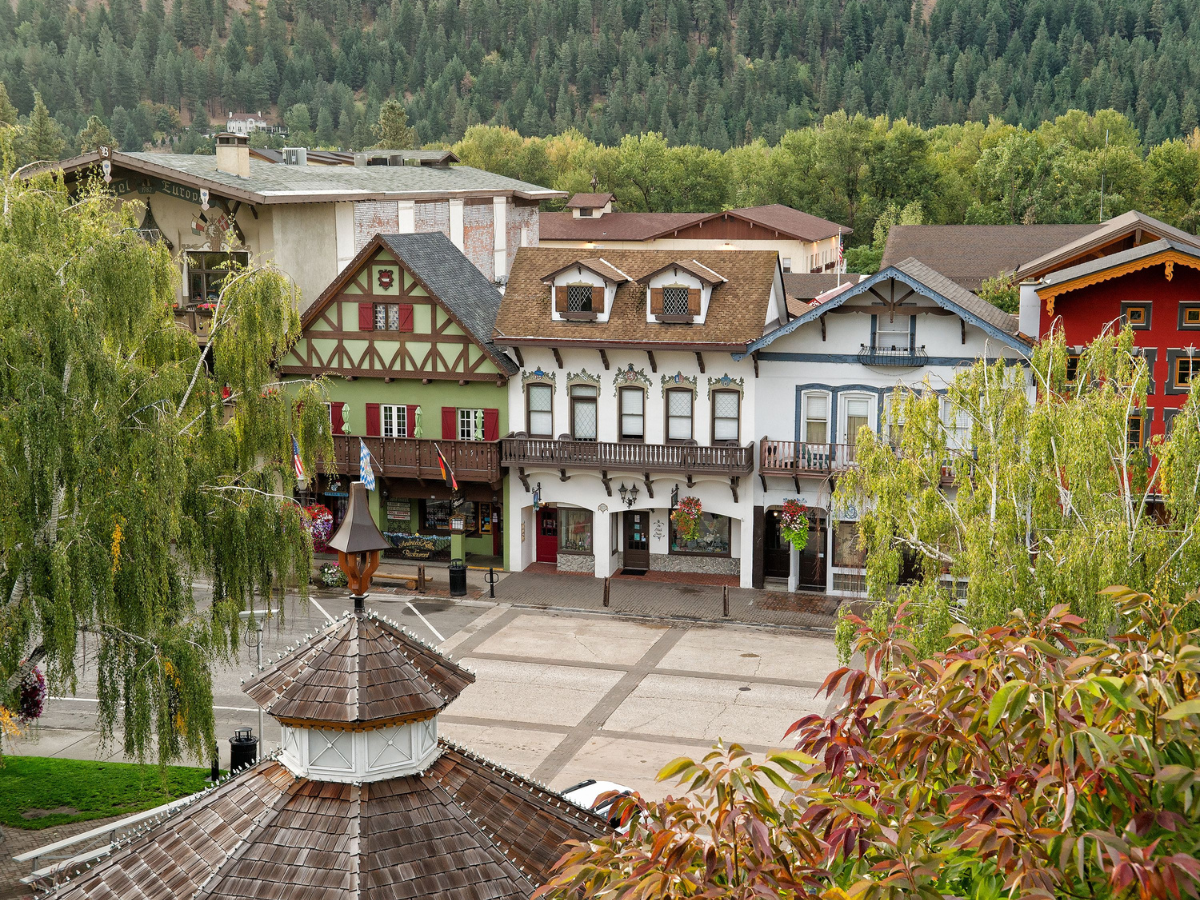 The charming Bavarian-style village of Leavenworth, Washington surrounded by lush greenery. The view includes colorful, Alpine-inspired buildings with timber accents, nestled in front of a backdrop of forested hills. The peaceful scene suggests a serene atmosphere, highlighting why this might be one of the best times to visit Leavenworth, especially during the changing seasons.