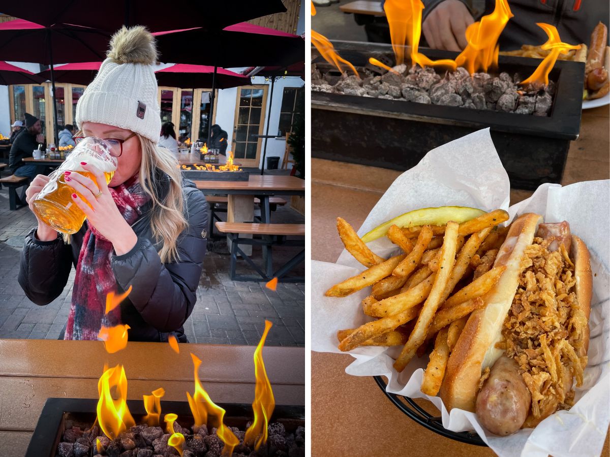 The image is split into two scenes. On the left, Kate from Kate's Crossing blog is seated outdoors in Leavenworth, Washington, enjoying a large glass of beer. She is bundled up in a white knit hat, plaid scarf, and winter jacket, sitting by a warm firepit on a cozy patio. On the right, a close-up shot of a hearty meal is shown: a sausage topped with crispy onions in a bun, served with seasoned fries and a pickle. Flames from the firepit can be seen in both images, adding to the warm, relaxed atmosphere.