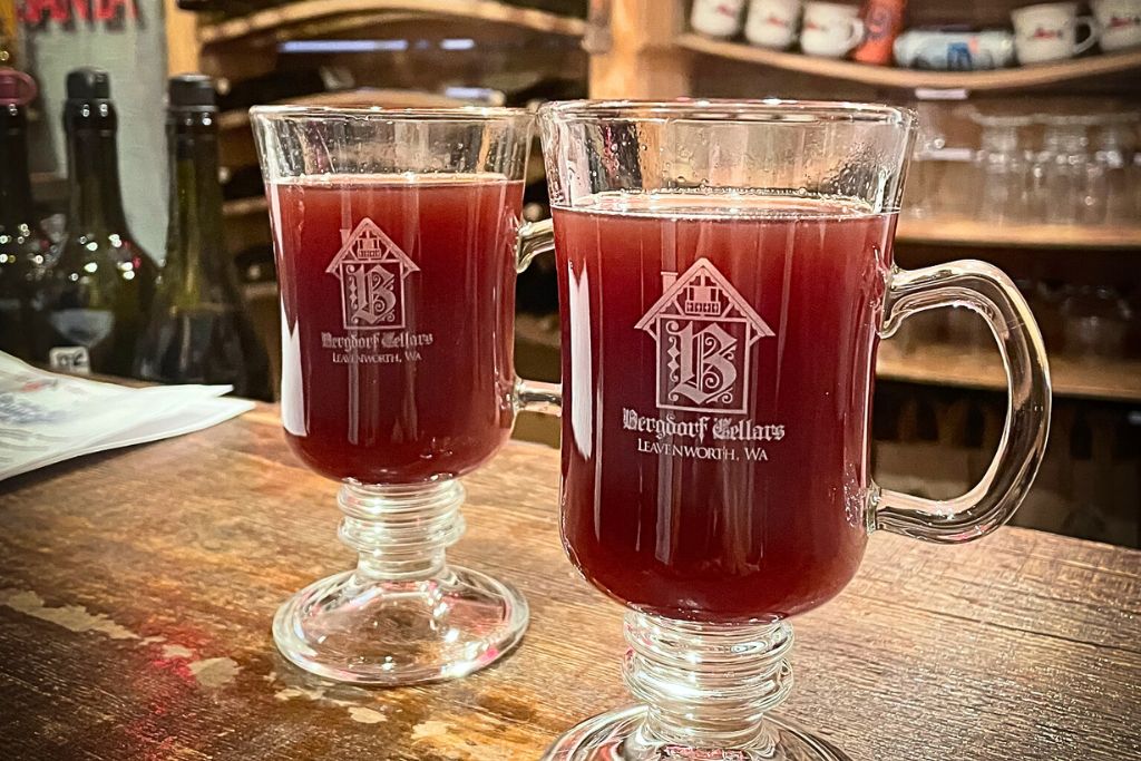 two glass mugs filled with warm mulled wine from Bergdorf Cellars in Leavenworth, WA. The rich red wine is served in branded mugs, set on a wooden counter in a cozy tasting room.