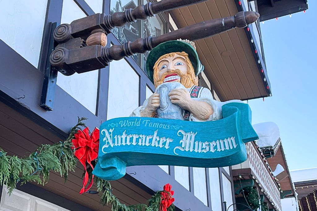 the whimsical sign for the "World Famous Nutcracker Museum" in Leavenworth, featuring a large nutcracker figure holding a mug. The building is decorated with festive greenery and red ribbons, enhancing the holiday feel. 