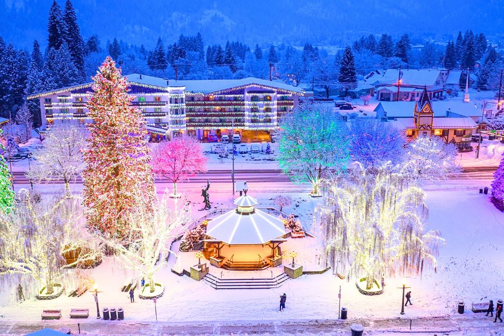 A breathtaking winter evening in Leavenworth, with vibrant holiday lights illuminating the trees, buildings, and a central gazebo in the town square. The snow-covered ground enhances the magical atmosphere, with colorful lights reflecting off the snow.