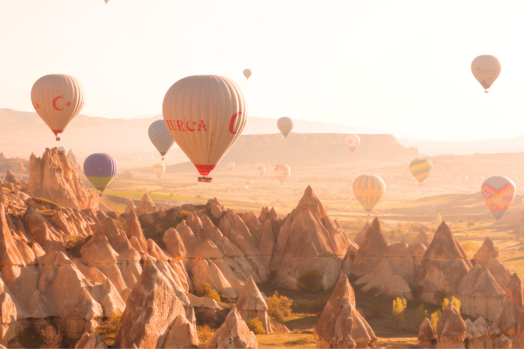 This image showcases the stunning landscape of Cappadocia, Turkey, with hot air balloons gracefully floating above its unique rock formations during a golden sunrise. The warm tones of the morning light illuminate the valleys and fairy chimneys, creating a magical and serene atmosphere.