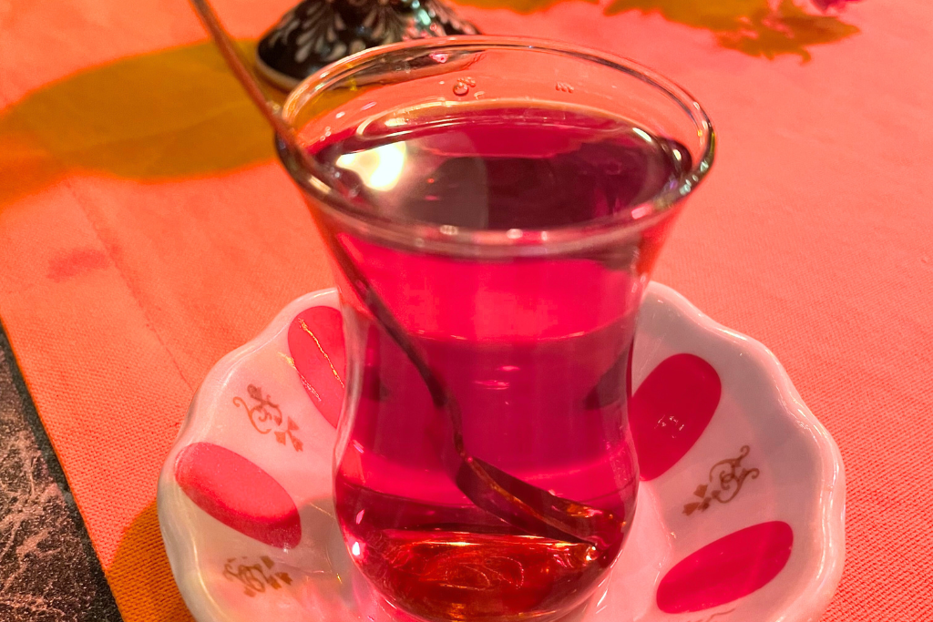 This image features a traditional Turkish tea served in a tulip-shaped glass with a small saucer, set on a vibrant tablecloth. The rich, warm color of the tea contrasts beautifully with the decorative patterns on the saucer.