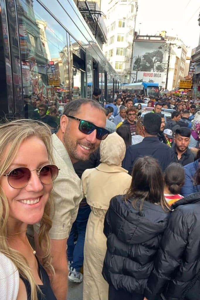 Kate and her husband smile for a selfie in a bustling street in Istanbul during the end of Ramadan celebrations. The crowded street scene captures the energy and cultural richness of the celebration.