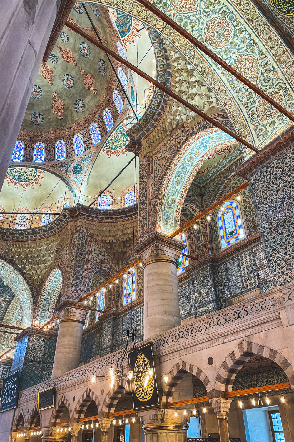 The intricate interior of the Blue Mosque in Istanbul, showcasing stunning domes, detailed floral patterns, vibrant stained-glass windows, and elegant Arabic calligraphy under soft ambient lighting.