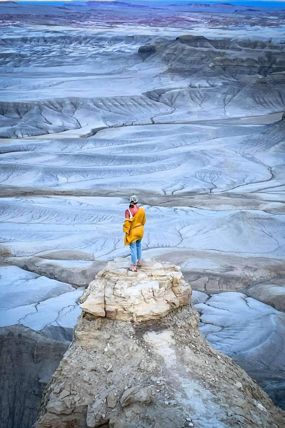 This image features Kate standing on a rocky ledge at Moonscape Overlook in Southern Utah. The desolate and surreal terrain of layered ridges and barren valleys extends in the background.