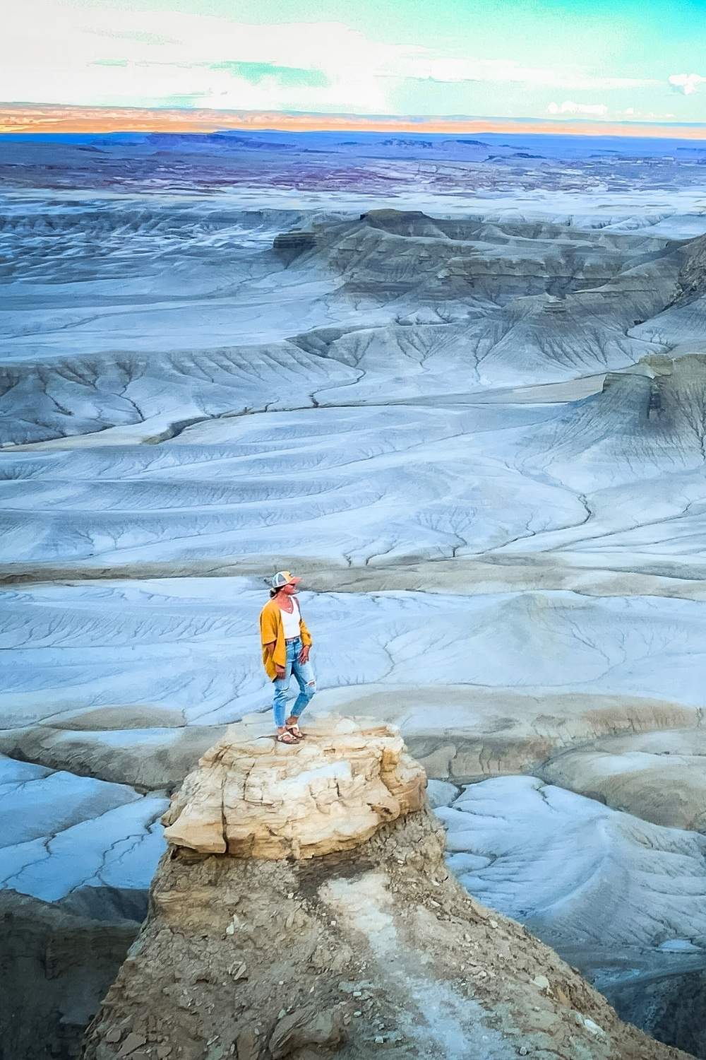 This image shows Kate standing on a rugged sandstone outcrop at Moonscape Overlook in Southern Utah. The barren, lunar-like terrain stretches out into the horizon, showcasing dramatic ridges and valleys under a soft gradient sky. It’s a striking depiction of the unique, otherworldly beauty of the American Southwest.