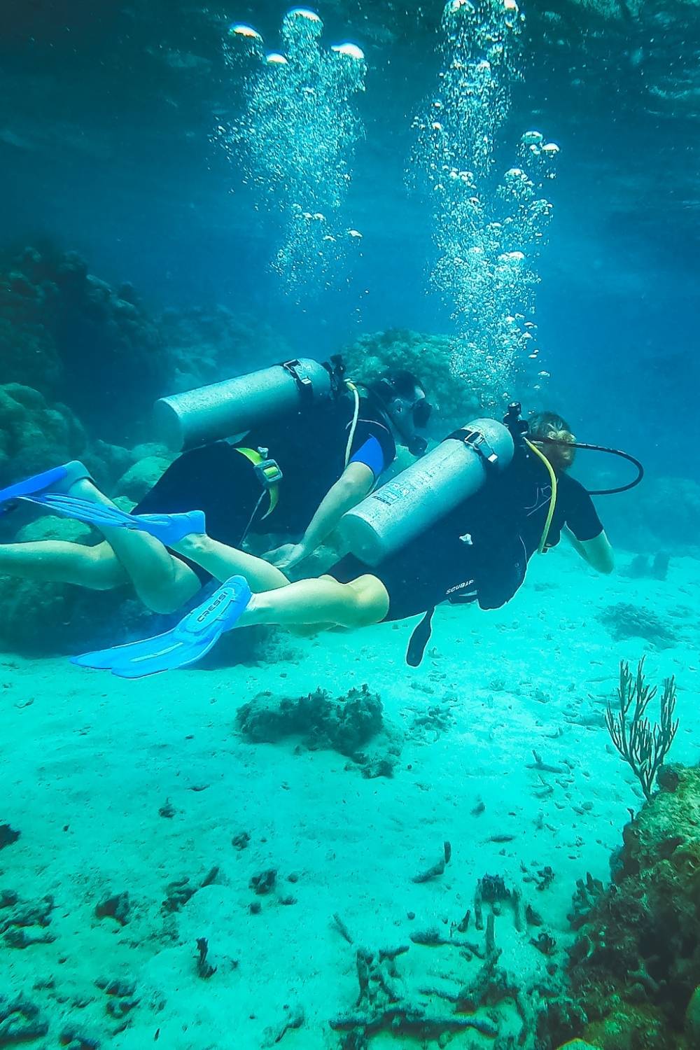 This photo shows Kate and her husband scuba diving side by side in Belize's turquoise waters, surrounded by coral reef. 