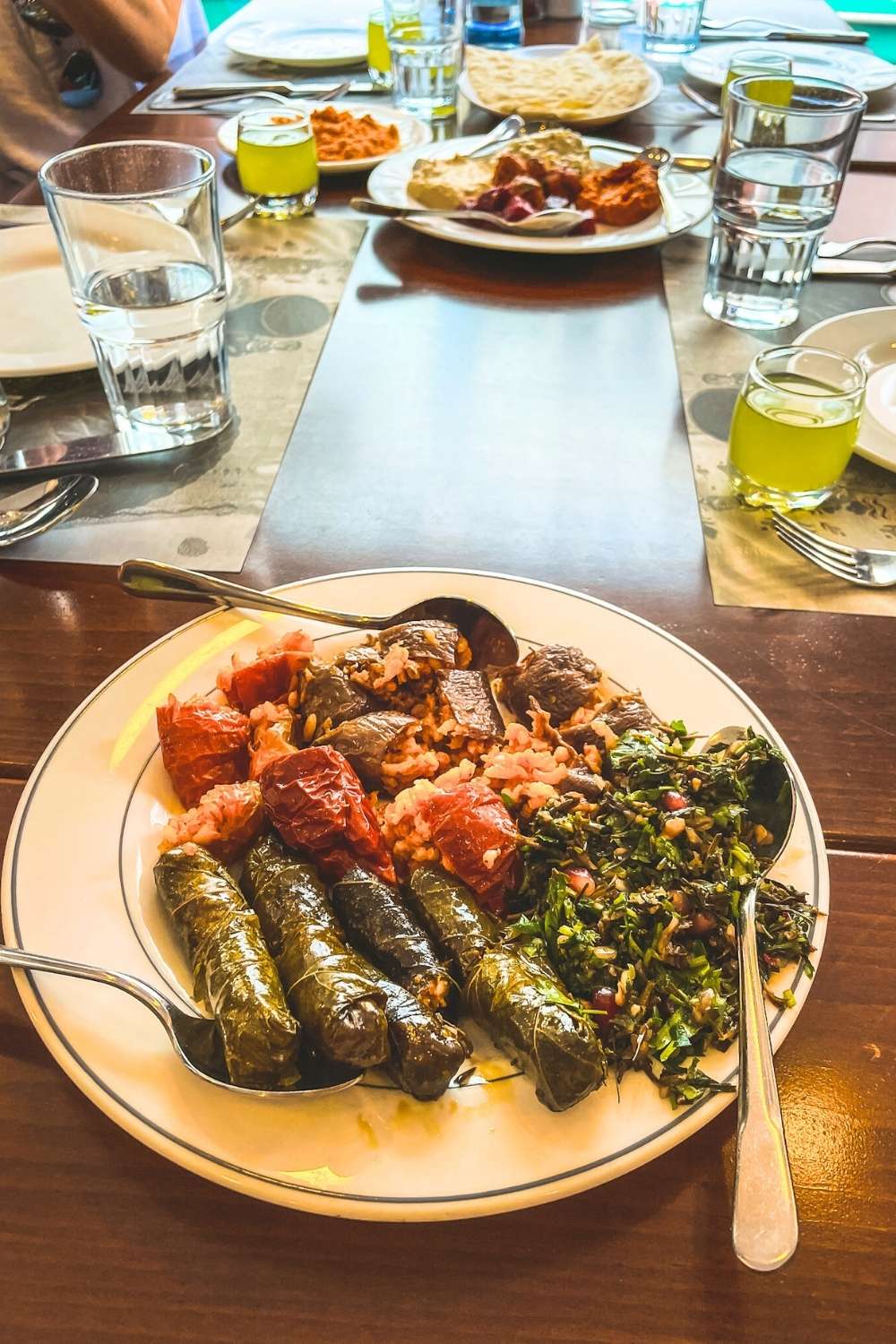 This image showcases a plate of traditional Turkish cuisine, featuring stuffed grape leaves (dolma), roasted vegetables, and a side of fresh parsley salad. The table is set with additional plates of dips, bread, and glasses of water, hinting at a communal dining experience during a food tour in Istanbul.