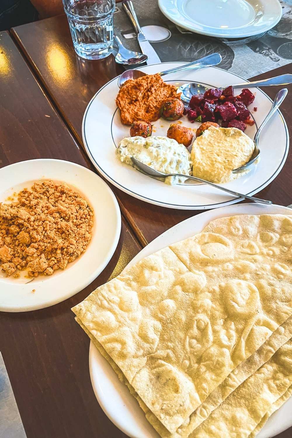 This image features a selection of Turkish appetizers, including creamy dips like hummus and tzatziki, a vibrant beet salad, spicy red pepper spread, and small meatballs. Alongside, there is a plate of flatbread and a dish of crumbled dessert, offering a balanced mix of savory and sweet flavors. The setup highlights the diverse and flavorful elements of Turkish cuisine.