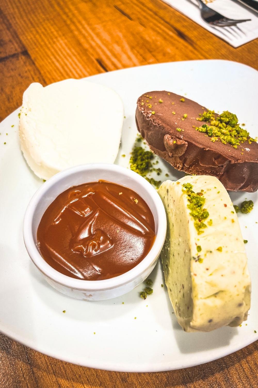 The image showcases a plate of Turkish ice cream, or "dondurma," with three distinct flavors, including plain, chocolate, and pistachio, garnished with crushed pistachios. Accompanied by a small dish of rich caramel sauce, this traditional dessert highlights the creamy and chewy texture that sets Turkish ice cream apart.