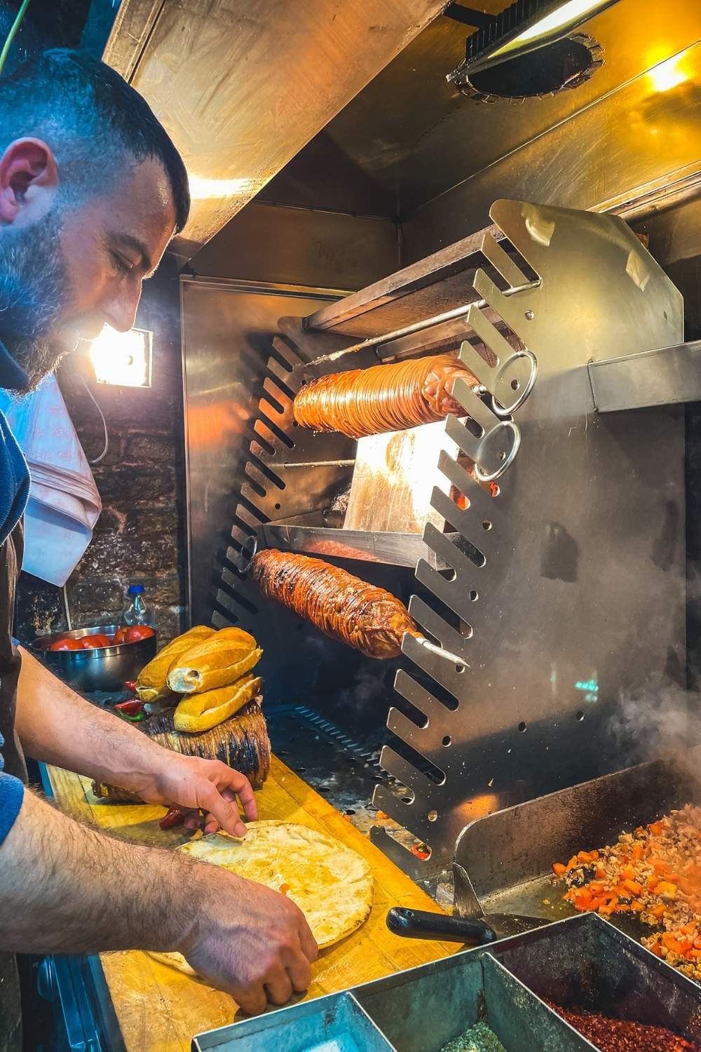 The image captures a vendor preparing kokoreç, a popular Istanbul street food made from grilled lamb intestines, inside a food stall. The sizzling rotisserie, fresh bread, and chopped ingredients on the counter emphasize the authentic and flavorful culinary experience of Istanbul's vibrant street food scene.