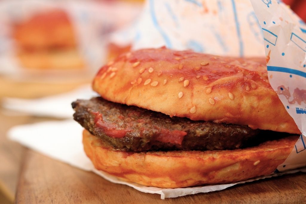 The image features a close-up of a Turkish wet burger (Islak Burger), a small burger soaked in a tangy tomato and garlic sauce, wrapped in wax paper.