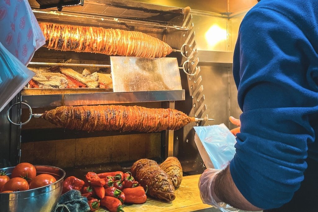 The image shows a scene with a vendor preparing kokoreç, a popular Istanbul street food made from grilled seasoned lamb intestines, with colorful vegetables displayed below. The setup highlights the vibrant and authentic culinary culture of Istanbul's streets, perfect for food enthusiasts.