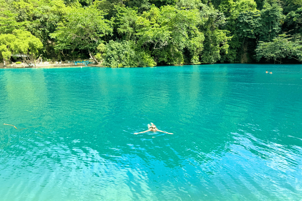 Kate floats peacefully in vibrant turquoise water surrounded by lush green forest at the Blue Lagoon in Jamaica.