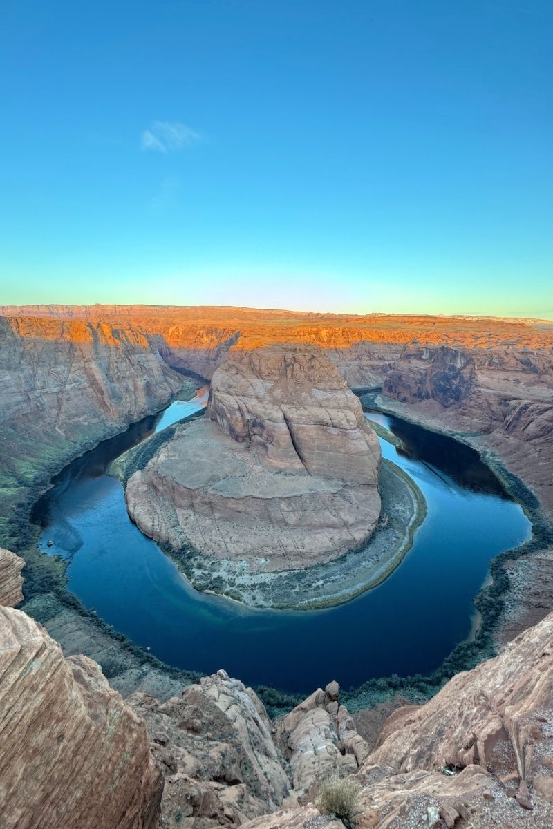 A stunning view of Horseshoe Bend near Page, Arizona, with the Colorado River curving around a massive rock formation at sunrise, casting golden light on the canyon walls.