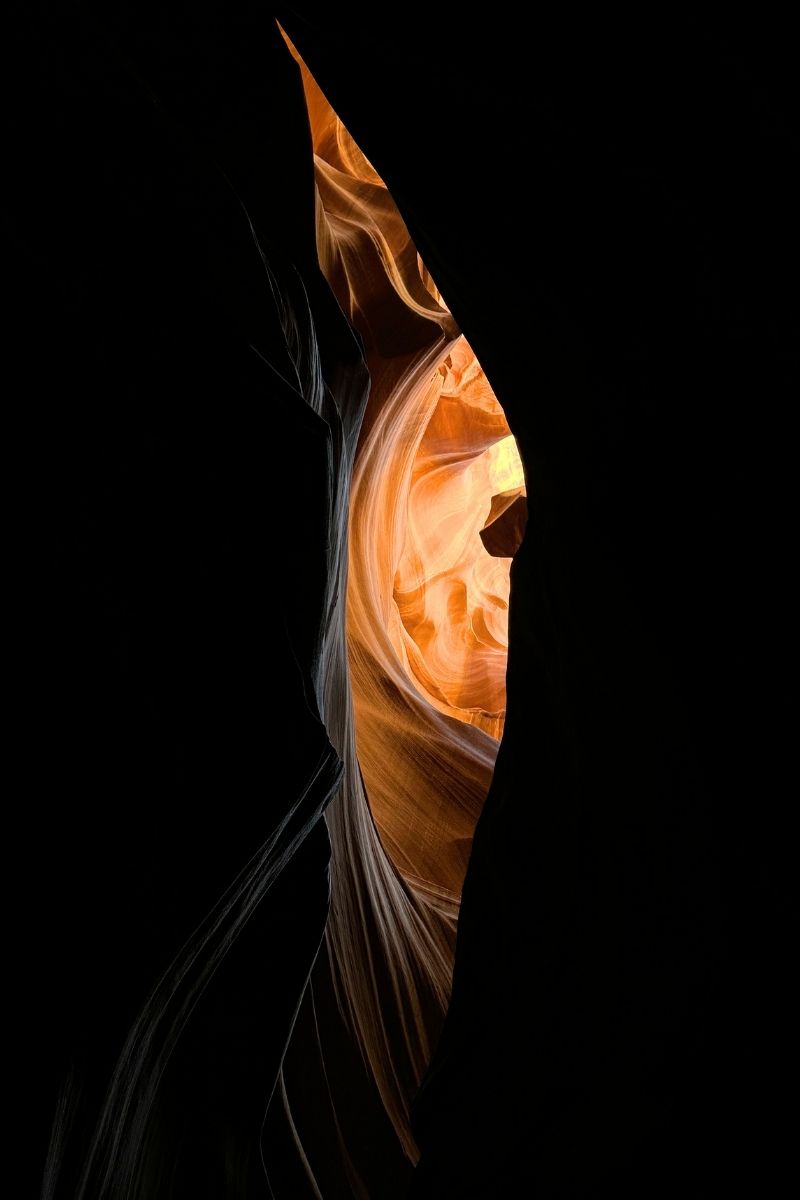 A beam of golden light illuminates the flowing sandstone walls of Upper Antelope Canyon near Page, Arizona, revealing intricate textures and curves in an otherwise shadowy slot canyon.