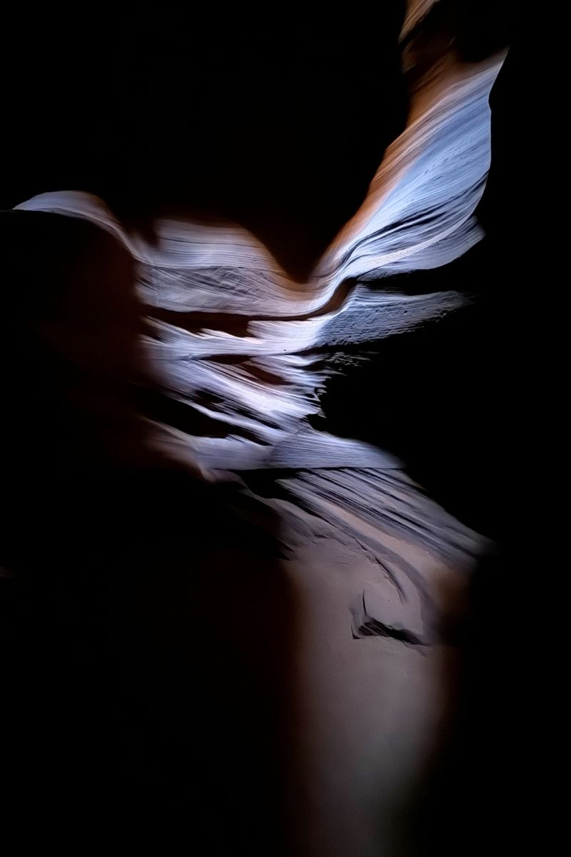 A naturally sculpted hummingbird shape appears in the sandstone wall of Upper Antelope Canyon, softly lit by a narrow beam of light that reveals the delicate textures and curves against the surrounding darkness.
