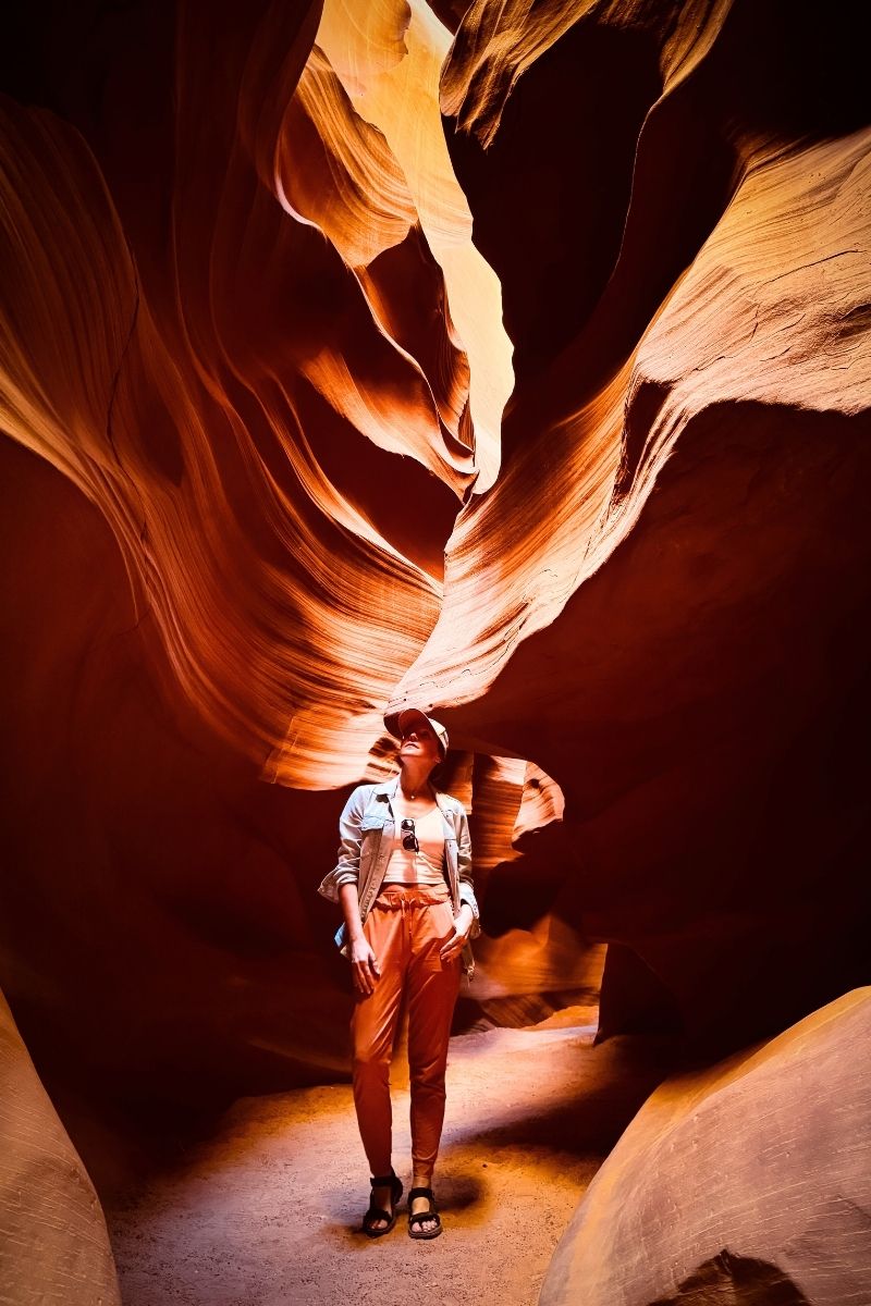 Kate stands beneath the swirling sandstone curves of Upper Antelope Canyon, bathed in warm golden light streaming through the narrow canyon walls above her.
