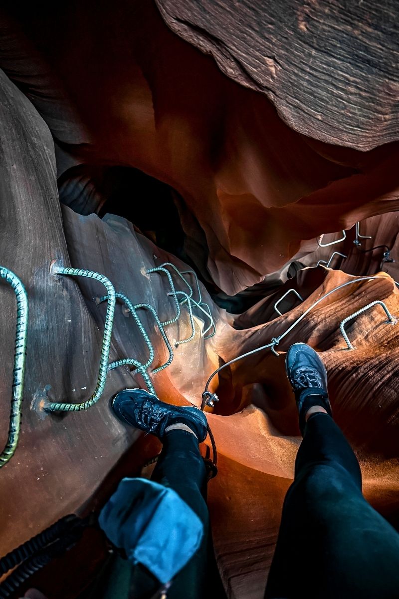 A climber’s perspective looking down a steep metal ladder bolted into the curving sandstone walls of a narrow slot canyon at Antelope Ridge Adventure Park in Arizona.