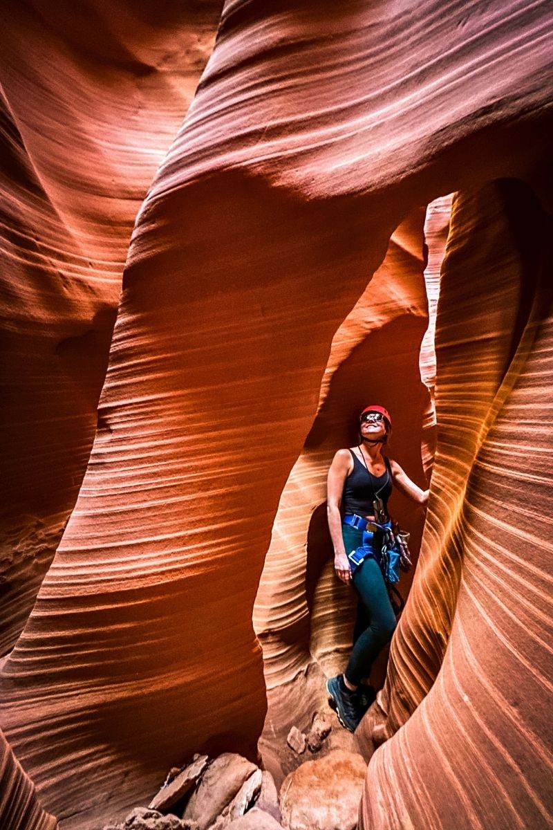 Kate pauses mid-adventure inside a glowing slot canyon at Antelope Ridge Adventure Park, surrounded by swirling sandstone walls and wearing climbing gear with a red helmet and harness.
