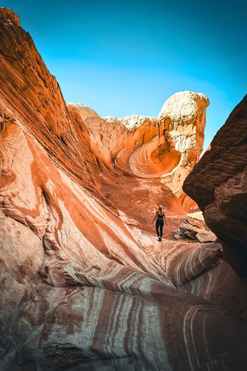 Kate hikes through the surreal, ribbon-striped sandstone landscape of White Pocket in Vermilion Cliffs National Monument, surrounded by dramatic rock swirls and bold desert colors.