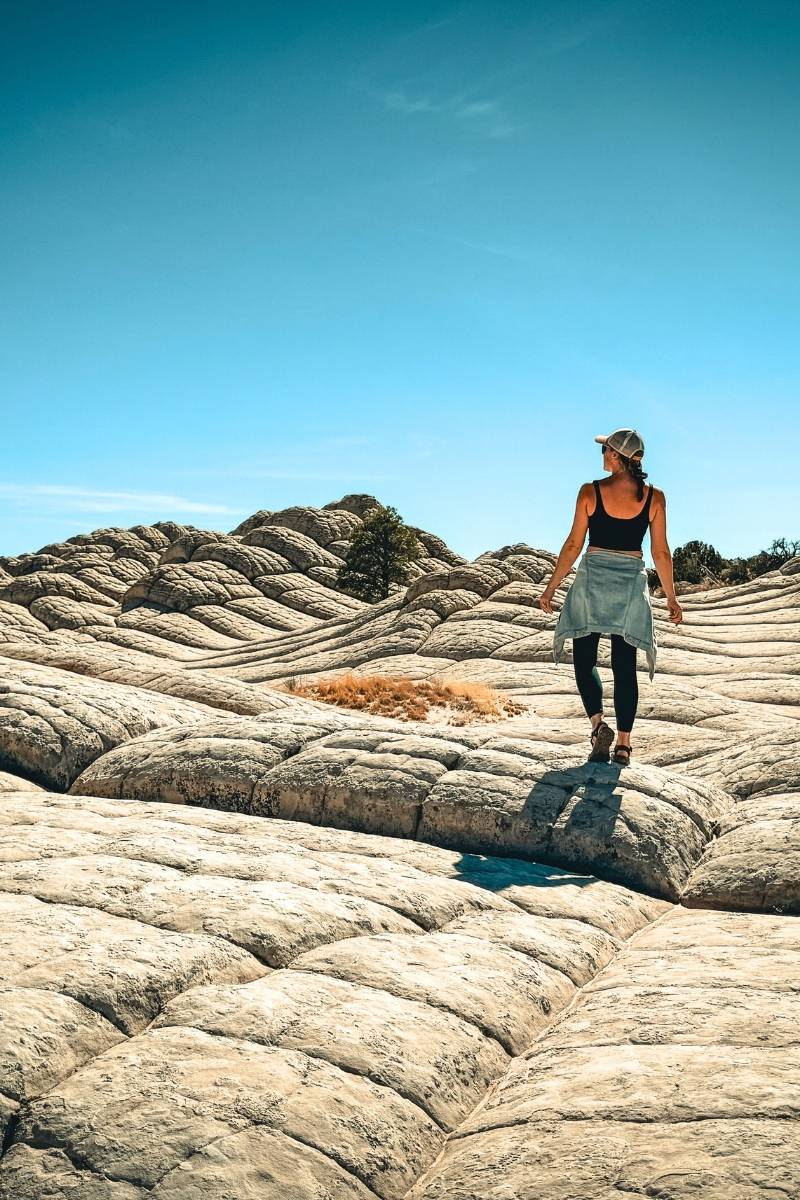 Kate walks across the unique, brain-like rock formations of White Pocket in Vermilion Cliffs National Monument, surrounded by rolling textures and bright desert sky.