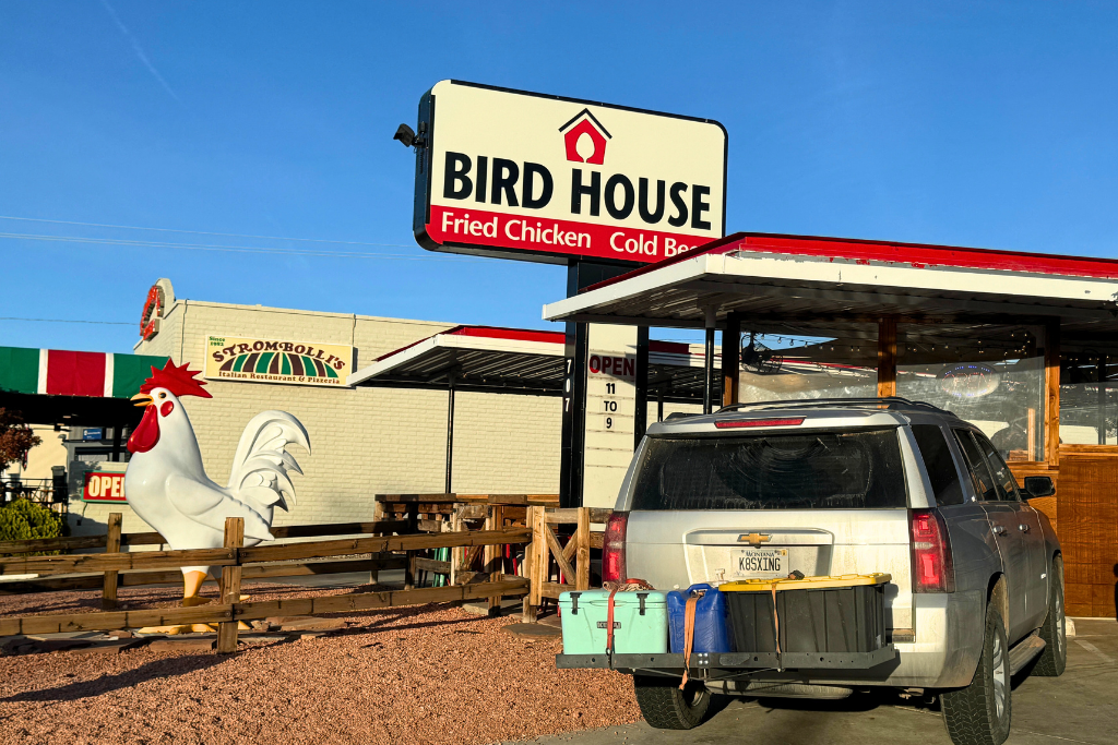 Exterior of The Bird House restaurant in Page, Arizona, featuring a sign that reads “Bird House – Fried Chicken Cold Beer,” a giant white rooster statue near the entrance.