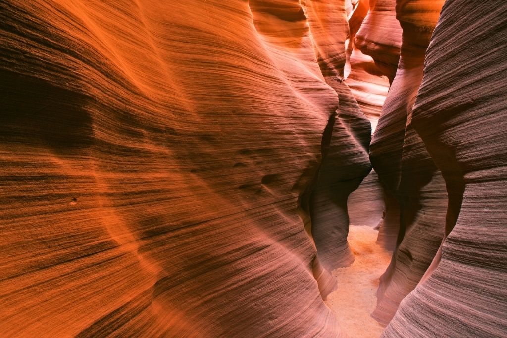 The winding, narrow passage of Waterholes Canyon near Page, Arizona, glows with rich orange and purple hues, showcasing smooth, layered sandstone walls shaped by centuries of erosion.