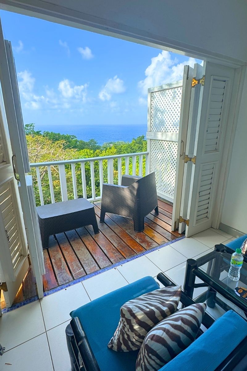 Cozy balcony seating with ocean views, seen through open white French doors in a bright tropical room with zebra-striped pillows and blue cushions.