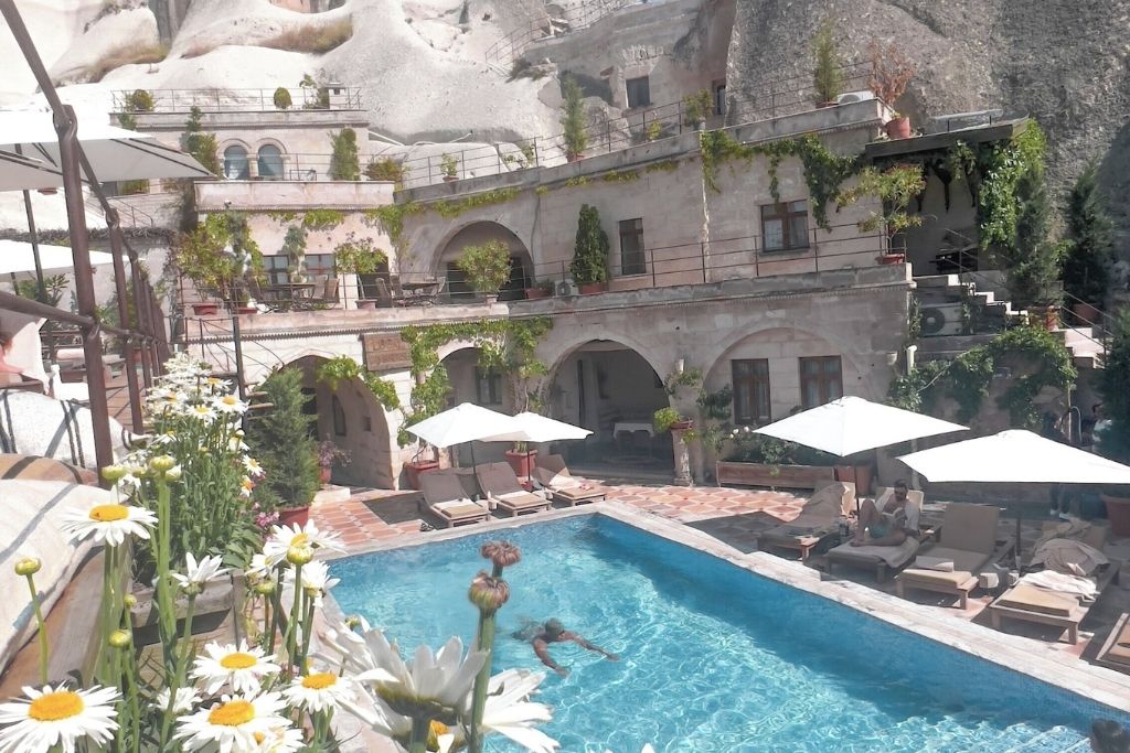 The turquoise pool of Local Cave House Hotel in Cappadocia, surrounded by sun loungers, white umbrellas, and terraces draped in greenery against the carved rock landscape.