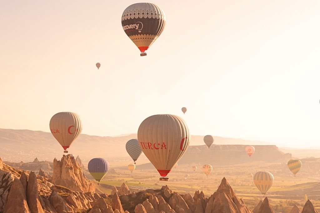 Hot air balloons drift above Cappadocia’s rocky landscape at sunrise, with soft golden light casting long shadows over the valley.