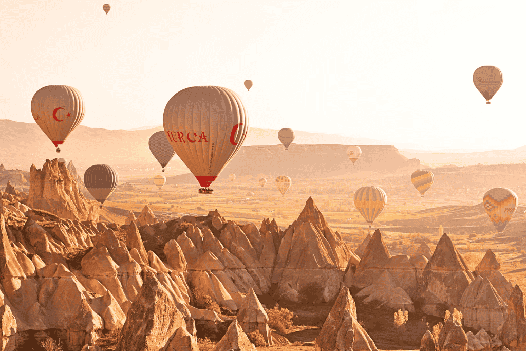 Dozens of hot air balloons float over Cappadocia’s unique rock formations at sunrise, casting a golden glow across the valley.