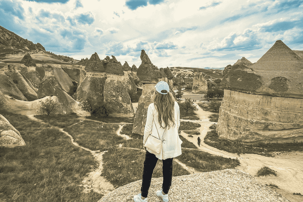 Kate stands on a rocky overlook in Cappadocia, gazing out at the surreal fairy chimneys and winding trails below under a partly cloudy sky.