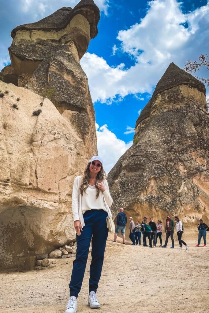 Kate smiles while standing in Monks Valley (Pasabag) in Cappadocia, surrounded by towering fairy chimneys and other visitors exploring the unique rock formations.