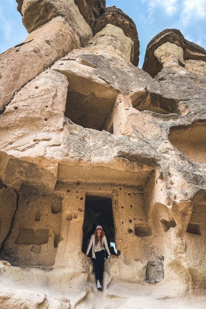 Kate steps out of a carved doorway in one of the towering fairy chimneys of Monks Valley in Cappadocia, surrounded by honeycombed rock walls and ancient openings.