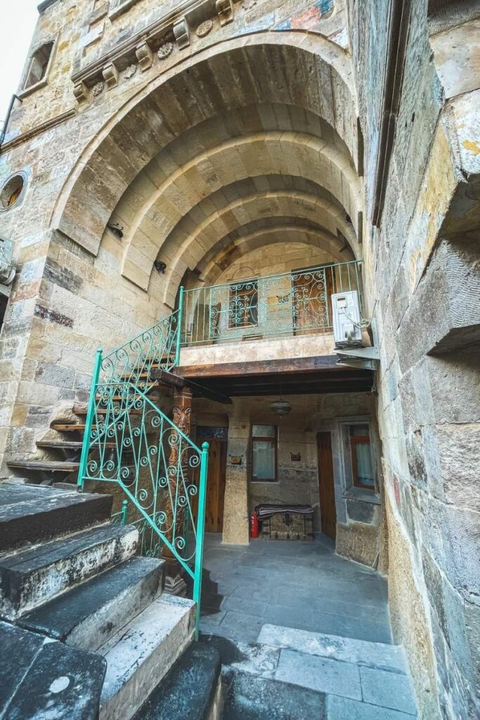 The arched stone entrance and turquoise iron staircase of Terra Cave Hotel in Cappadocia showcase its historic charm and unique cave-style architecture.