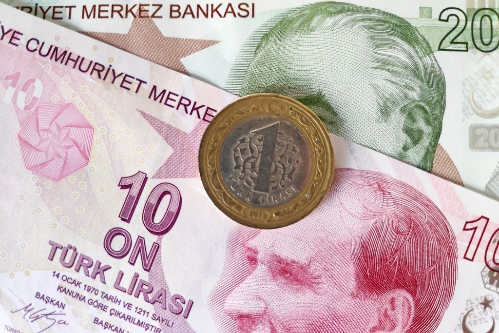 Close-up of Turkish currency featuring a 1 lira coin placed over colorful 10 and 20 lira banknotes, each with portraits of Mustafa Kemal Atatürk.