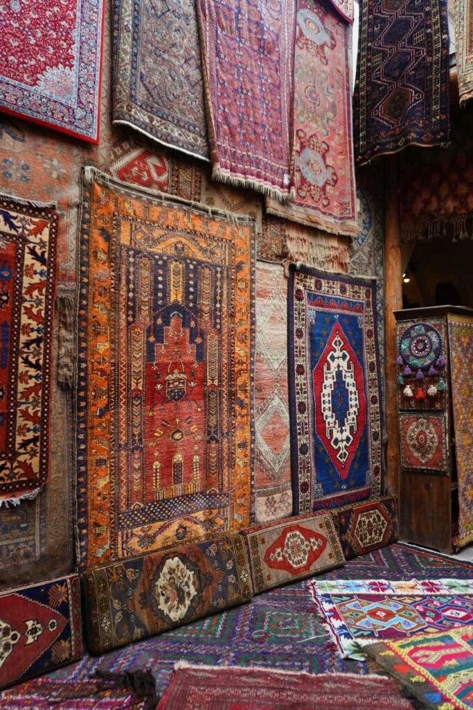 A vibrant display of traditional Turkish carpets in rich reds, blues, and oranges hangs and layers across a shop wall in Cappadocia.