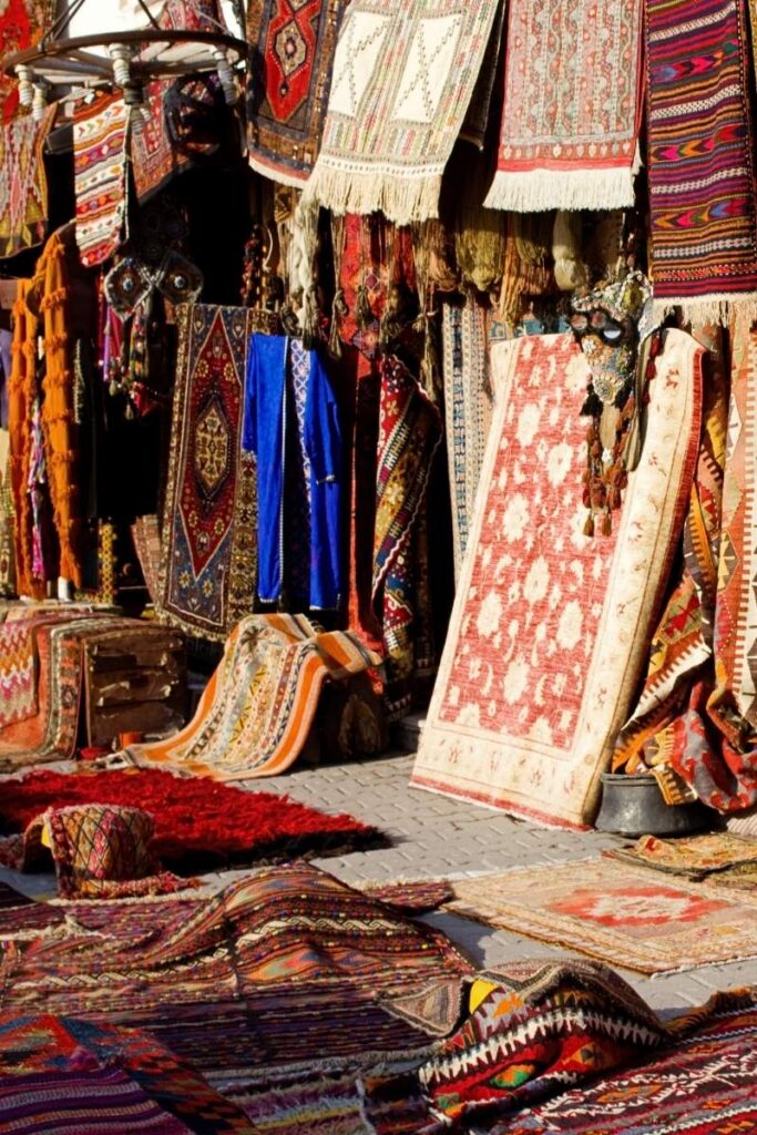 A colorful street display in Cappadocia showcases layered Turkish rugs, textiles, and wall hangings in bold patterns and rich earthy tones.