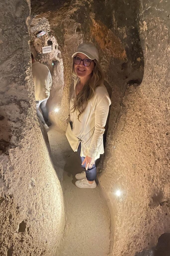 Kate smiles while carefully navigating a narrow, dimly lit tunnel inside Cappadocia’s ancient underground city.