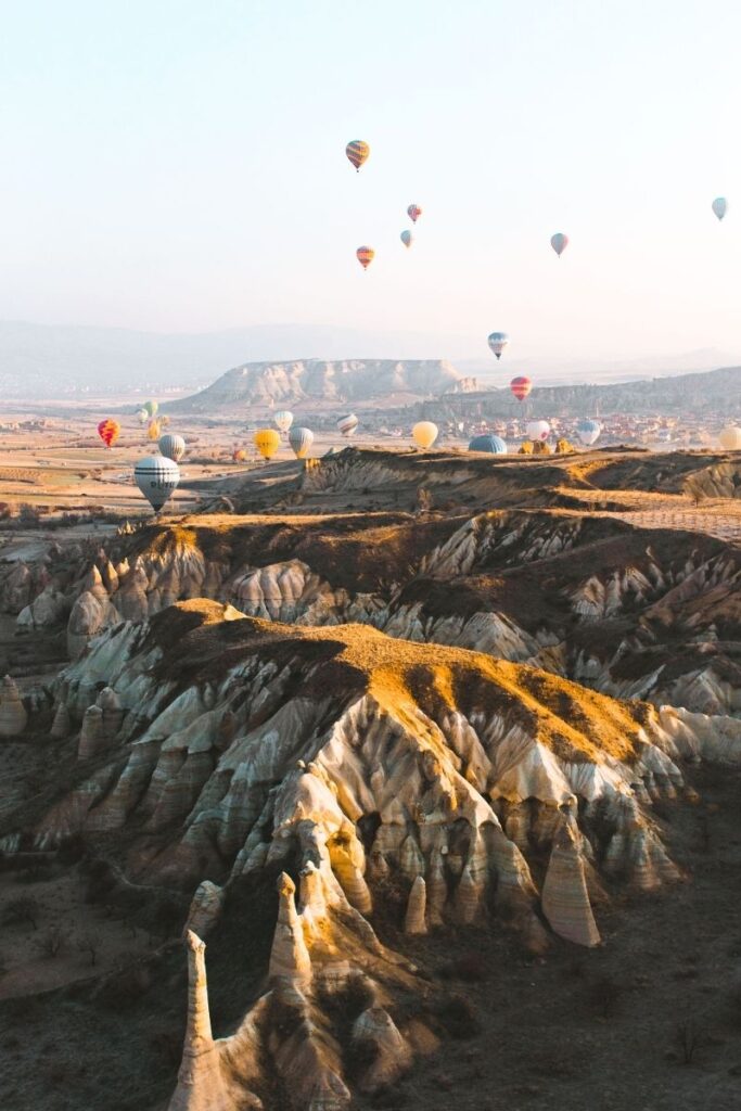 Hot air balloons float over Cappadocia’s sunlit, striped rock ridges and valleys, creating a dreamy sunrise landscape across the Turkish countryside.