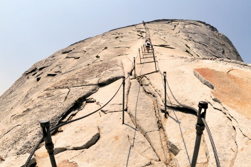 View looking up the steep granite slope of Half Dome, with hikers ascending using the metal cable system anchored into the rock.