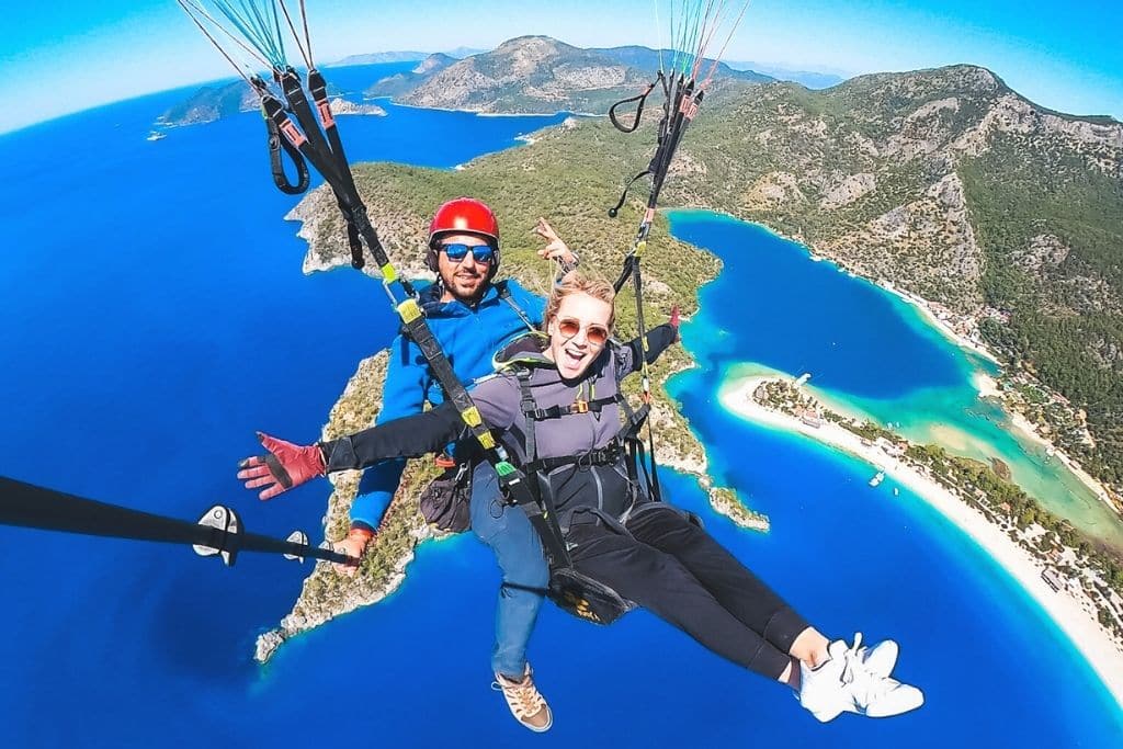 Kate soars over the vivid blue lagoon and lush mountains of Ölüdeniz, Turkey, while paragliding with a guide and beaming with excitement.