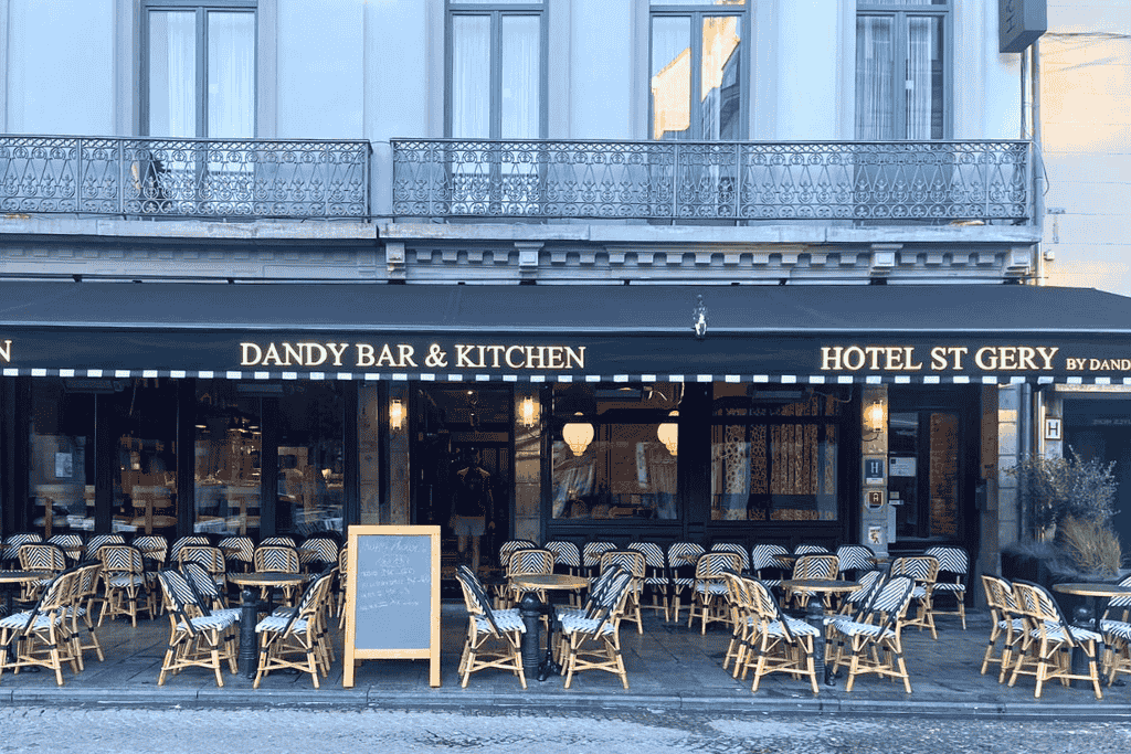 Outdoor seating lines the front of Dandy Bar & Kitchen at Hotel St. Gery in Brussels, with black-and-white striped chairs arranged neatly under a matching awning.
