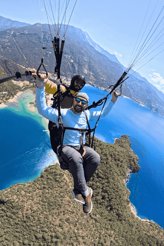 Kate’s husband beams with excitement while paragliding high above the lush coastline and mountain ridges of Ölüdeniz, Turkey, with the shimmering lagoon far below.
