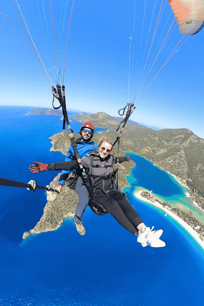 With arms outstretched, Kate floats in tandem over the dazzling Blue Lagoon in Ölüdeniz, framed by turquoise waters and lush mountains below.