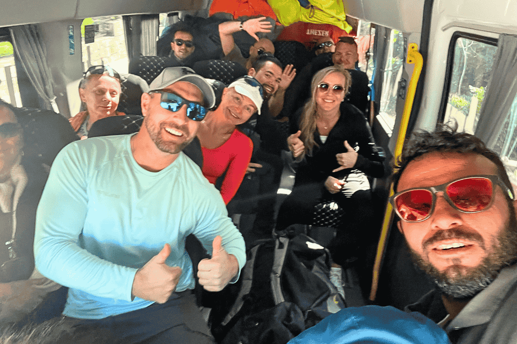 Kate and a cheerful group of paragliders smile and give thumbs up inside a minibus heading up the mountain for their Ölüdeniz paragliding adventure.