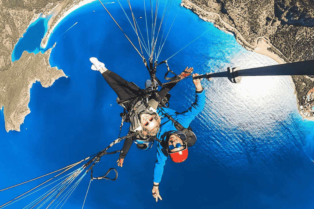 Kate tandem paraglides high above Ölüdeniz’s iconic Blue Lagoon, smiling wide with her arms outstretched over the deep turquoise coastline.